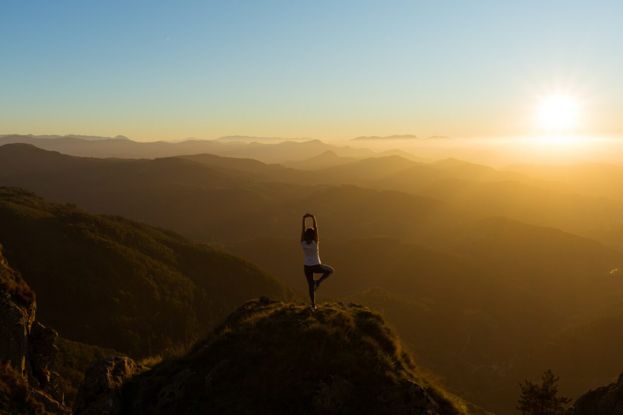 Una mujer meditando en la cima de una montaña en medio de la nada.