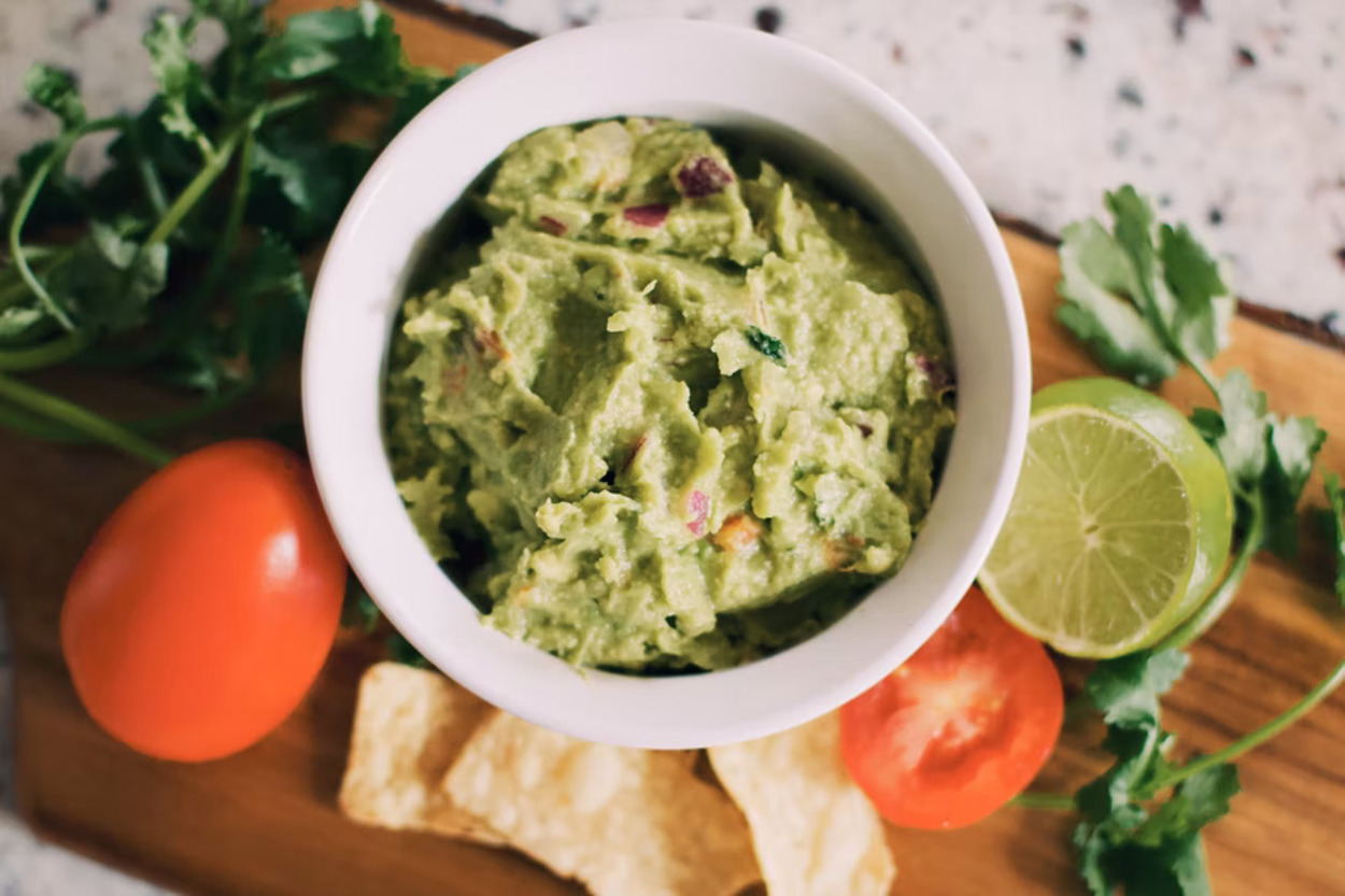 Un bol de guacamole junto a sus ingredientes principales