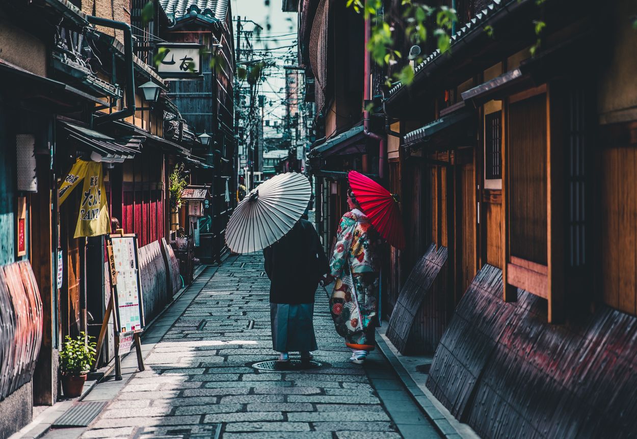 Dos personas caminando por un callejón estrecho con sombrillas