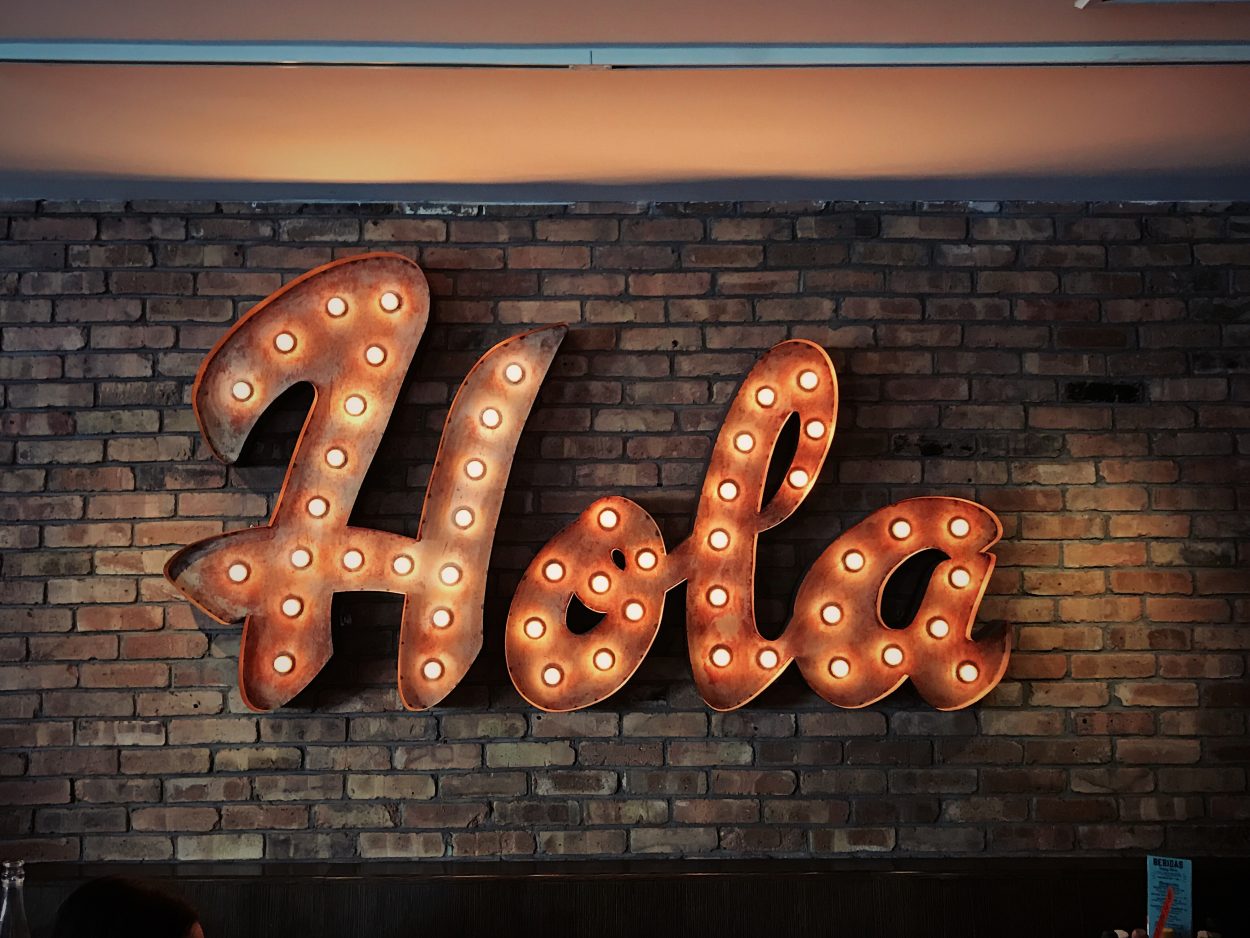 Una pared de ladrillo que tiene está decorada con la palabra española 'Hola'