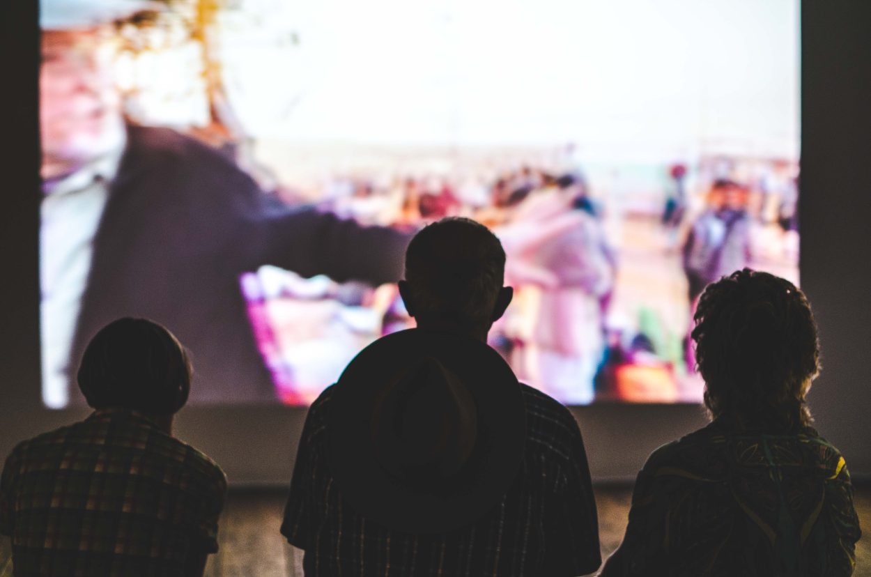 Una película se muestra en una pantalla grande y tres personas la están viendo.
