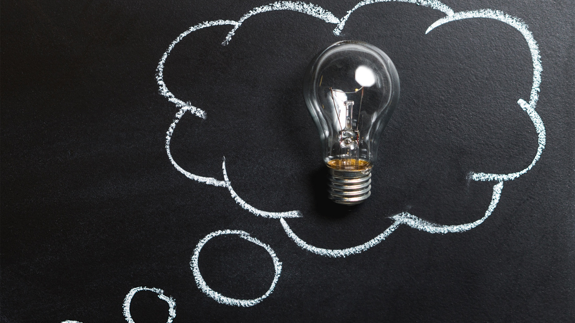 una bombilla en una pizarra con un dibujo de una burbuja de pensamiento