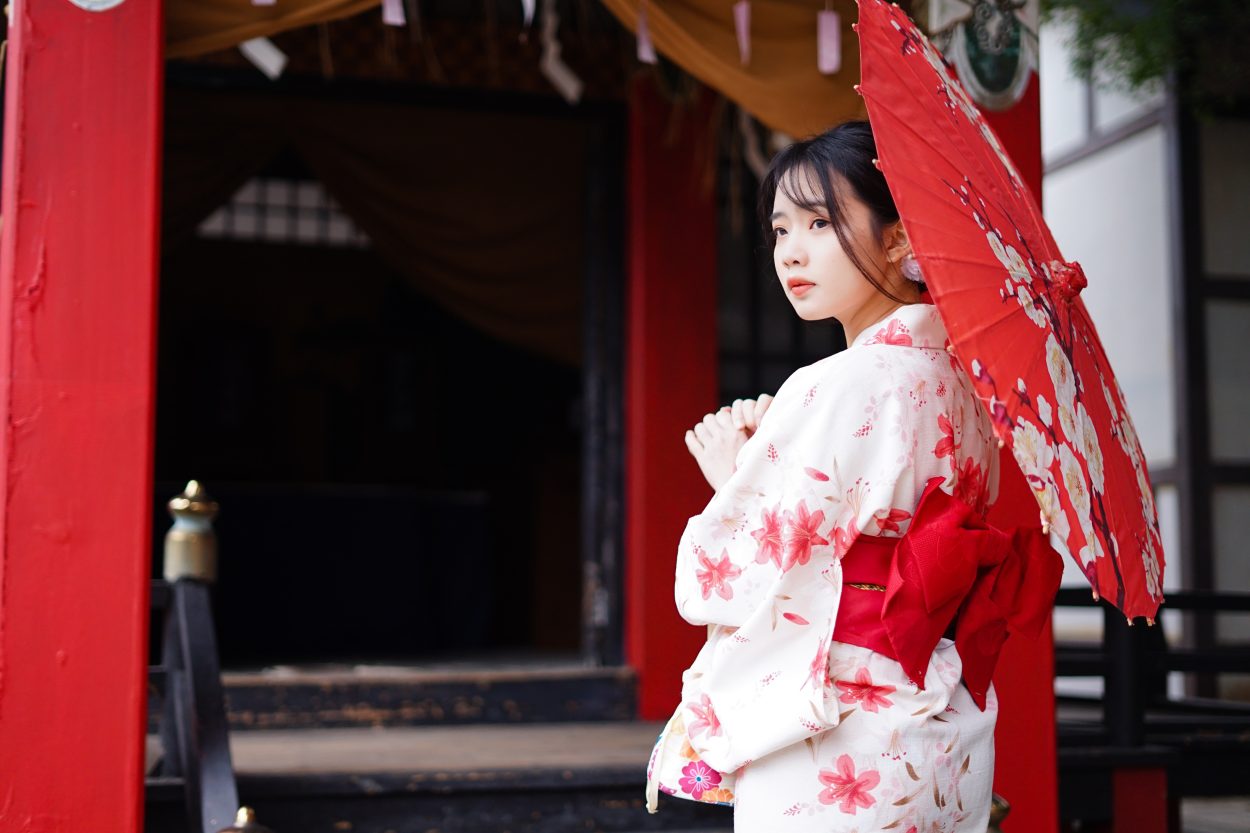 Una mujer vestida con ropa tradicional japonesa sosteniendo una sombrilla de papel de color rojo tradicional 