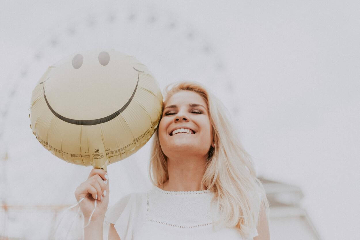 Imagen de una mujer sonriendo mientras sostiene un globo en la mano.