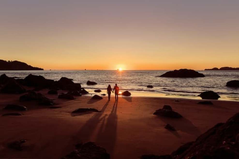 Una imagen de una pareja en una playa con la puesta de sol también capturada